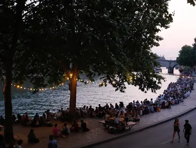 Orang-orang duduk saat berkumpul di tepi sungai Seine sebagai bagian dari acara musim panas Paris Plages di Paris, Prancis (7/7). (AFP Photo/Francois Guillot)
