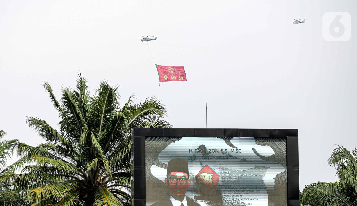 Helikopter TNI AU mengibarkan bendera Trimatra raksasa di kawasan Gedung DPR RI, Jakarta, Selasa (5/10/2021). TNI AU mengerahkan enam helikopter yang membawa bendera Merah Putih serta bendera Trimatra raksasa. (Liputan6.com/Faizal Fanani)