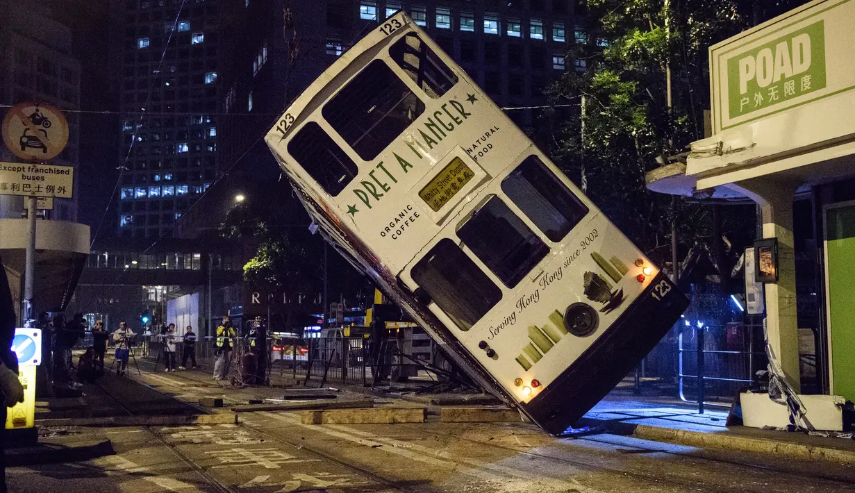 Sebuah trem double-decker diangkat menggunakan crane setelah terbalik di jalan utama di Hong Kong, Kamis (6/4). Kecelakaan yang terjadi tengah malam waktu setempat itu mengakibatkan 11 orang mengalami luka-luka. (ANTHONY WALLACE / AFP)