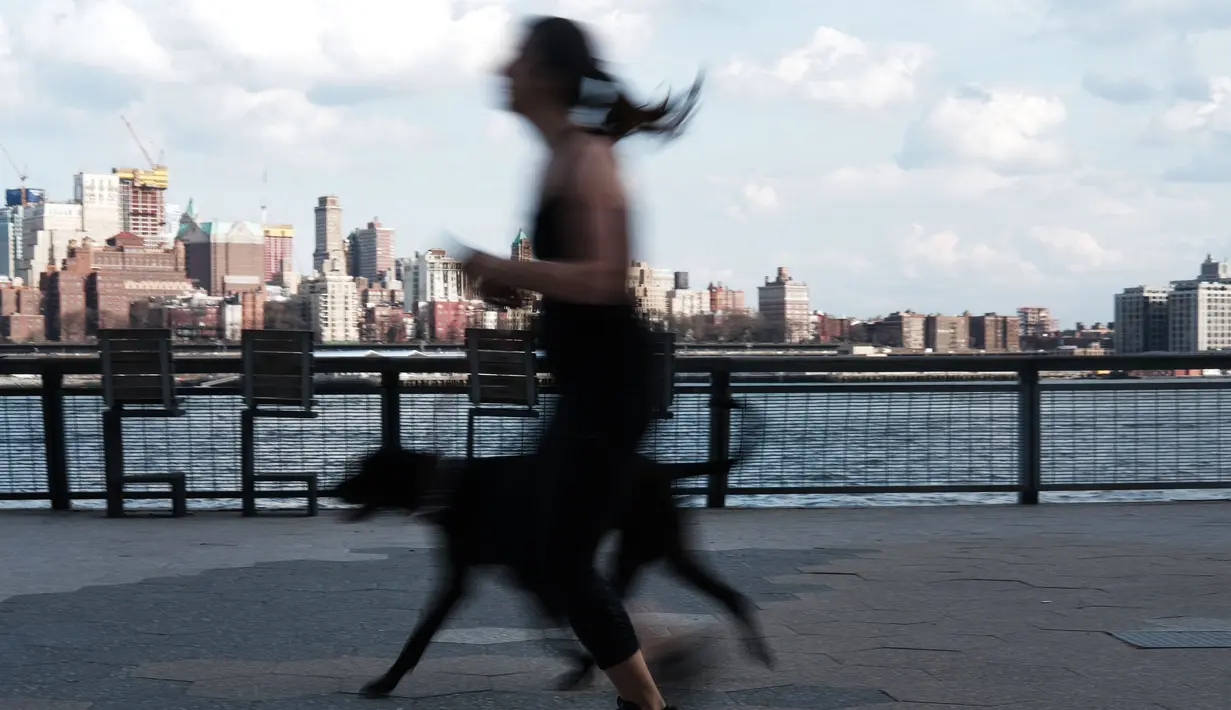 Seorang wanita bersama anjingnya berlari selama musim semi yang hangat di tepi air di Manhattan di New York City (8/4). Sebagian besar Pantai Timur mengharapkan suhu hangat terus sepanjang minggu. (Spencer Platt/Getty Images/AFP)