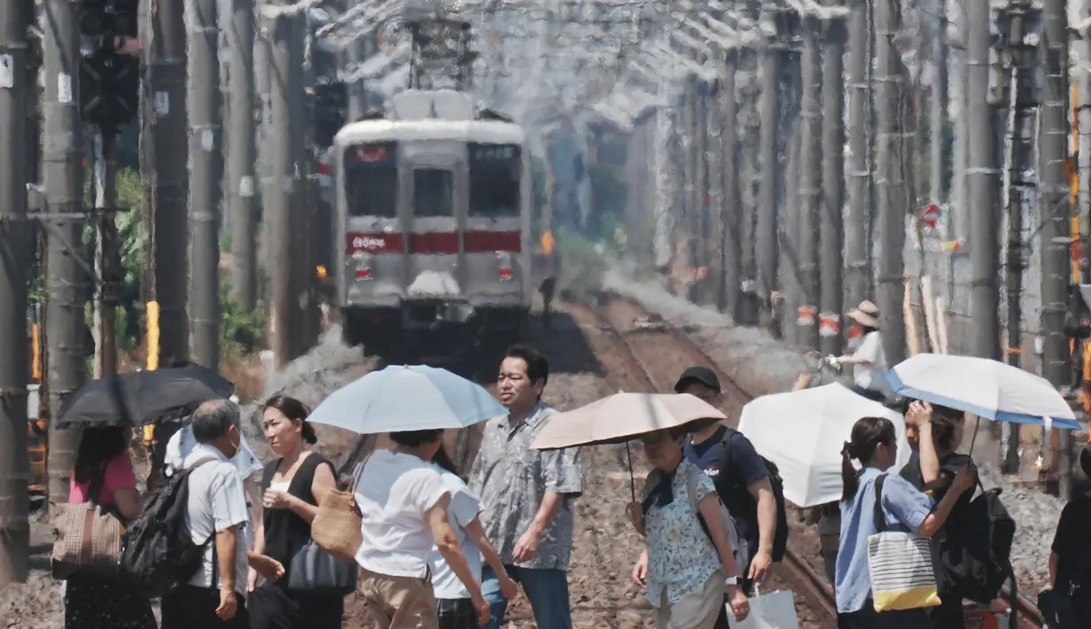 Peringatan cuaca panas ekstrem telah dikeluarkan di 44 dari total 47 prefektur di Jepang. Tampak dalam foto, kabut panas terlihat di latar belakang saat pejalan kaki dengan payung melintasi rel kereta api di Tokyo pada 5 Agustus 2025. (Kazuhiro NOGI/AFP)