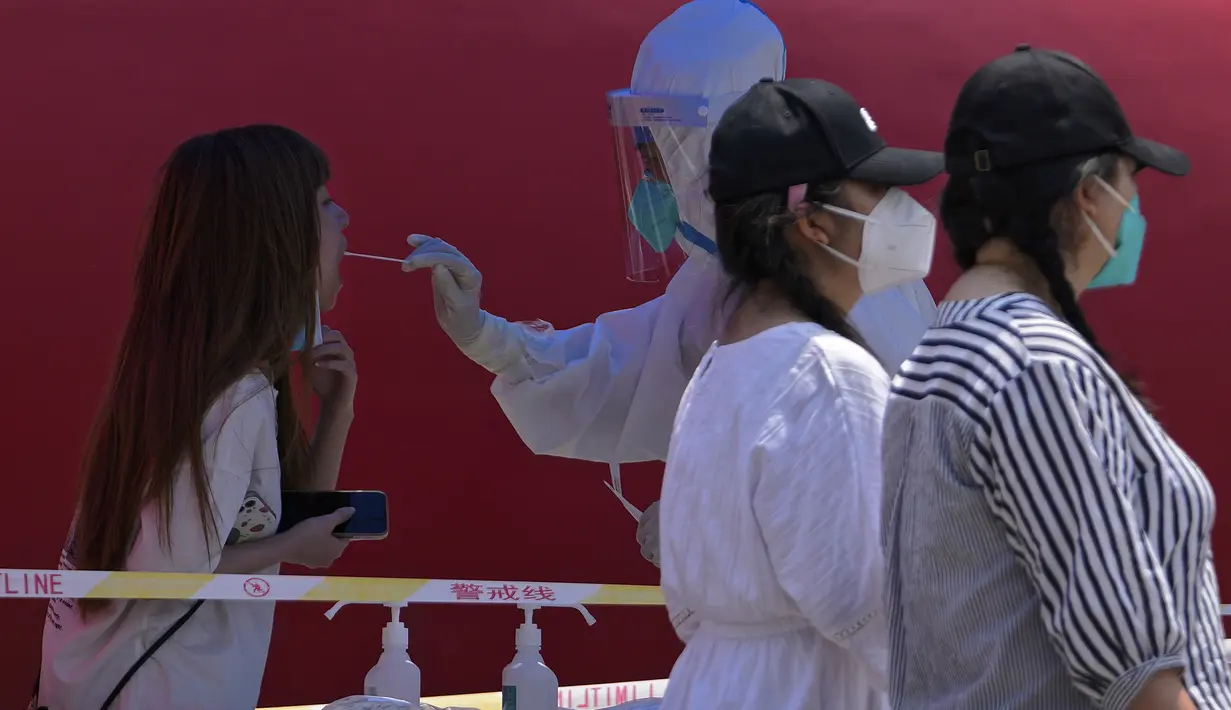 Warga yang mengenakan masker berjalan melewati seorang perempuan yang diambil swab tenggorokannya selama tes COVID publik di Beijing pada Senin, 23 Mei 2022. Beijing memperpanjang perintah bagi pekerja dan siswa untuk tinggal di rumah dan memerintahkan pengujian massal tambahan pada hari Senin untuk membendung kasus COVID-19 yang kembali meningkat di ibu kota China. (AP Photo/Andy Wong)