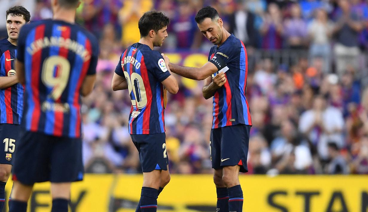 Gelandang Barcelona, Sergi Roberto (kedua kanan) menerima ban kapten dari Sergio Busquets pada laga Liga Spanyol 2022/2023 di Camp Nou Stadium, Barcelona (28/5/2023). Sergi Roberto merupakan gelandang jebolan La Masia yang dipromosikan ke tim utama Barcelona sejak awal musim 2013/2014. Hingga kini ia telah tampil dalam 348 laga di semua ajang dengan torehan 16 gol dan 40 assist. (AFP/Pau Barrena)