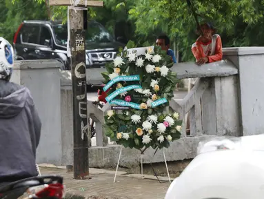 Warga berdiri dekat karangan bunga yang bersandar pada tiang lampu yang ditabrak mobil yang ditumpangi Ketua DPR Setya Novanto di Jalan Permata Berlian, Jakarta, Sabtu (18/11). Dalam karangan bunga tersebut tertulis pesan. (Liputan6.com/Angga Yuniar)