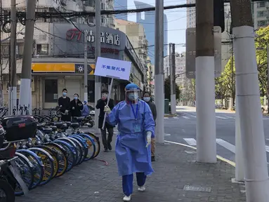 Pekerja dengan alat pelindung memegang tanda bertuliskan "Jangan berkerumun" selama hari pengujian massal bagi penduduk di distrik Jingan, Shanghai barat (4/4/2022). China telah mengirim lebih dari 10.000 petugas kesehatan ke Shanghai, termasuk 2.000 staf medis militer. (AP Photo/Chen Si)