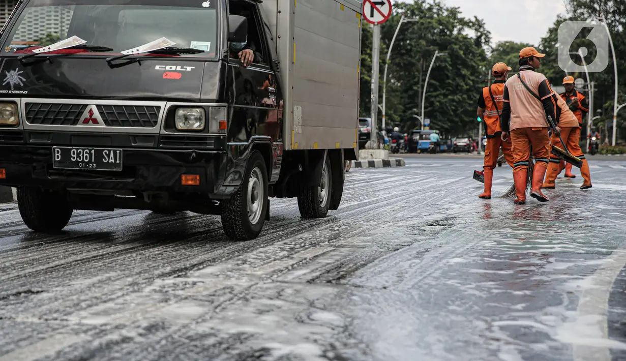 Mobil melewati jalan berbusa yang sedang dibersihkan anggota PPSU di kawasan Jalan Thamrin, Jakarta, Selasa (4/10/2022). Pembersihan ini akibat adanya tumpahan oli yang tercecer dijalan. (Liputan6.com/Faizal Fanani)