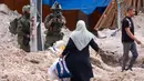 Seorang tentara Israel mengangkat senapannya saat warga Palestina membawa barang-barang mereka setelah diperintahkan untuk meninggalkan rumah mereka selama operasi Israel di kamp pengungsi Tulkarem di barat laut Tepi Barat yang diduduki pada 2 Mei 2025. (Jaafar ASHTIYEH/AFP)