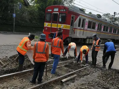 Kereta Commuter Line melintas di sebelah para pekerja yang sedang melakukan perawatan rutin rel kereta api di Manggarai, Jakarta, Selasa (11/7). (Liputan6.com/Helmi Afandi)