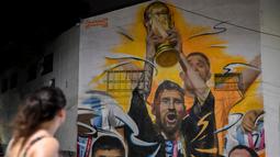 Warga melihat Mural yang menggambarkan kapten dan penyerang Argentina Lionel Messi mengangkat Trofi Piala Dunia 2022 di samping rekan satu timnya setelah memenangkan turnamen Piala Dunia Qatar 2022 di Buenos Aires pada 22 Desember 2022. Argentina berhasil meraih juara setelah mengalahkan Prancis di babak final. (AFP/Luis Robayo)