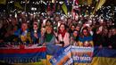 Orang-orang memegang plakat, bendera nasional Ukraina, dan menyalakan lampu ponsel mereka saat berkumpul untuk mendukung Ukraina yang menandai tahun ketiga invasi Rusia di Trafalgar Square, pusat kota London, pada 24 Februari 2025. (HENRY NICHOLLS/AFP)