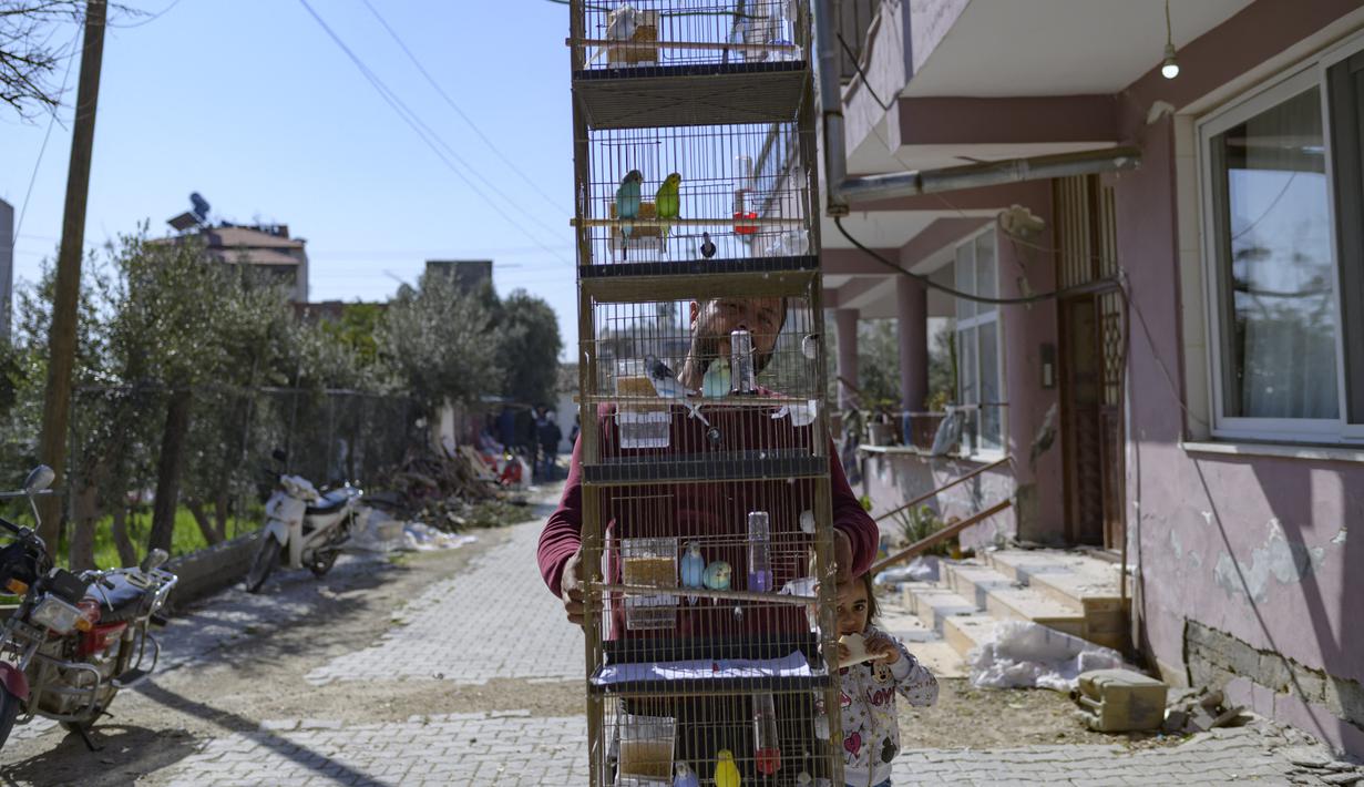 Seorang penduduk membawa burung dalam sangkar yang dia selamatkan dari rumahnya yang hancur di Samandag, selatan Hatay pada 16 Februari 2023, sepuluh hari setelah gempa berkekuatan 7,8 melanda wilayah perbatasan Turki dan Suriah. Banyak orang di kota Samandag di wilayah perbatasan Suriah mendengarkan kerabat dan teman mereka perlahan-lahan mati di bawah reruntuhan saat mereka menunggu penyelamat yang datang terlambat. (Photo by Yasin AKGUL / AFP)