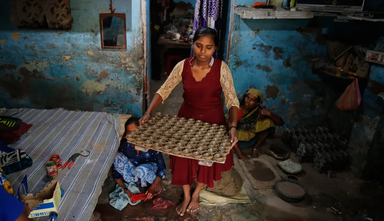Seorang pengrajin tembikar membawa lampu minyak yang terbuat dari tanah liat untuk dikeringkan menjelang festival Diwali di Prayagraj, India, Kamis (17/10/2019).  Diwali atau Deepavali merupakan festival lampu yang penting bagi umat Hindu di seluruh dunia. (AP/Rajesh Kumar Singh)
