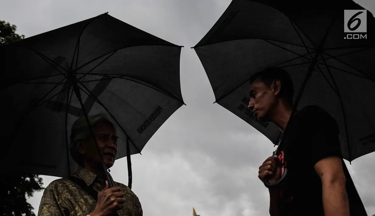 Aktivis Jaringan Solidaritas Korban untuk Keadilan (JSKK) membawa payung hitam saat menggelar aksi Kamisan ke-575 di depan Istana Merdeka, Jakarta, Kamis (21/2). Aktivis menolak kembalinya militer untuk menduduki jabatan sipil. (Liputan6.com/FaizalFanani)