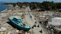Pengendara sepeda motor melewati perahu dan rerntuhan bangunan usai gempa dan tsunami melanda Palu, Sulawesi Tengah, Senin (1/10). Pihak berwenang tengah menyiapkan kuburan massal untuk memakamkan ratusan korban tewas. (JEWEL SAMAD/AFP)