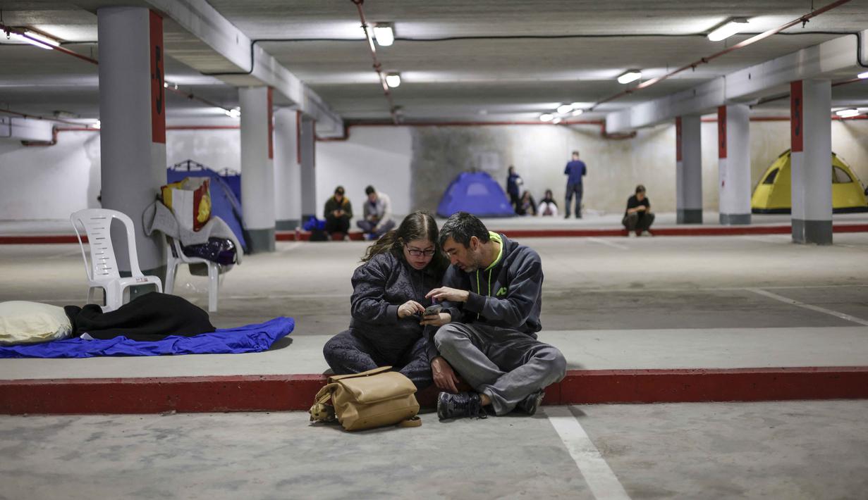 Warga Israel terpaksa melarikan diri ke bunker-bunker bawah tanah dan tempat perlindungan publik untuk menyelamatkan diri dari gelombang serangan rudal Iran. Tampak dalam foto, orang-orang berlindung di tempat parkir bawah tanah di Haifa pada Minggu 1 Maret 2026, di tengah kekhawatiran akan serangan Iran. (Jalaa MAREY/AFP)