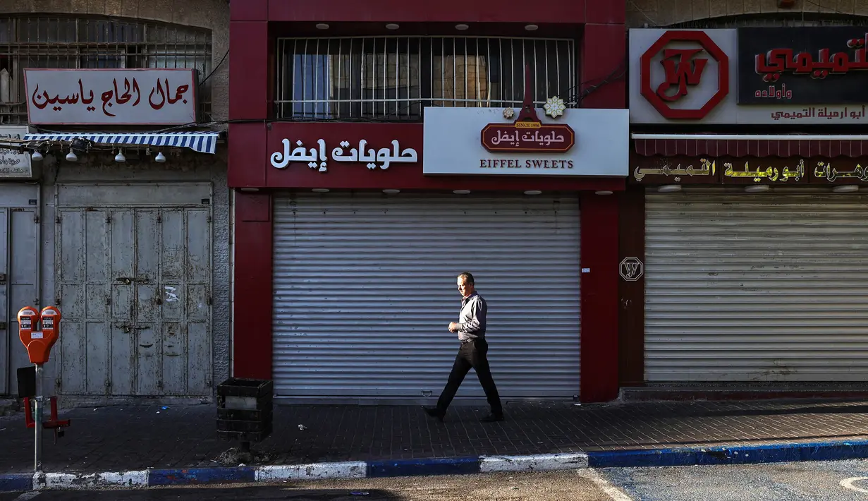 Seorang pria berjalan melewati toko-toko yang tutup selama pemogokan umum di Ramallah, sebelah barat laut kota itu di Tepi Barat, pada 11 Juni 2024. (Zain JAAFAR/AFP)
