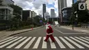 Pria berkostum Sinterklas menyeberang jalan saat membagikan kopi gratis kepada warga di kawasan Jalan Jenderal Sudirman, Jakarta, Sabtu (19/12/2020). Pembagian kopi tersebut bertujuan untuk menyambut perayaan Natal 2020. (Liputan6.com/Johan Tallo)