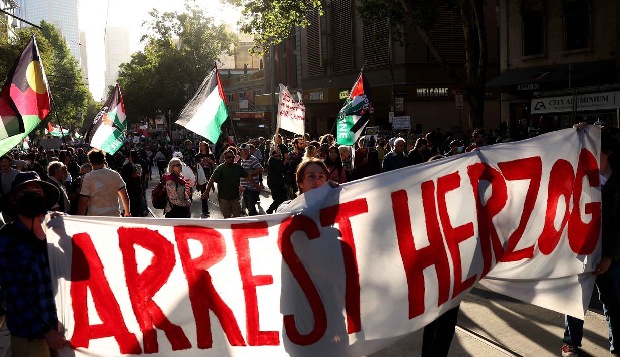 Para pengunjuk rasa membawa bendera Palestina dan berbagai spanduk yang menyuarakan penolakan terhadap kehadiran kepala negara tersebut. Tampak dalam foto, para pengunjuk rasa memegang plakat dan bendera saat mereka berunjuk rasa selama kunjungan Presiden Israel, Isaac Herzog, di Melbourne, Australia, pada Kamis 12 Februari 2026. (MARTIN KEEP/AFP)