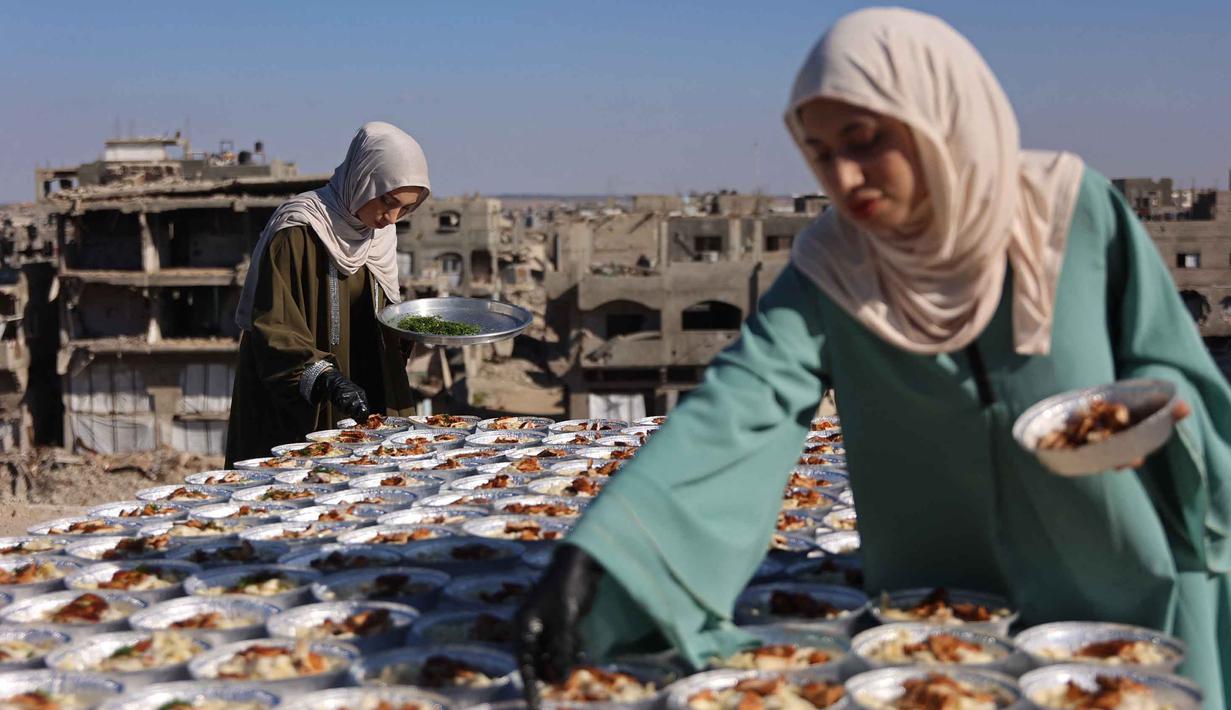 Kakak beradik Palestina, Lina Zeid (kanan) dan Aya Zeid, menyiapkan piring makanan di atap rumah mereka untuk dibagikan kepada anak-anak pengungsi sebagai kegiatan amal di daerah Al-Tuam, sebelah barat Jabalia, Jalur Gaza Utara pada Rabu 6 Mei 2026. (Omar AL-QATTAA/AFP)