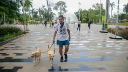 Wisatawan membawa dua ekor anjing saat mengunjungi Senayan Park, Jakarta, Rabu (9/12/2020). Libur Nasional Pilkada Serentak 2020 dimanfaatkan sebagian warga Jakarta dan sekitarnya untuk mengunjungi tempat rekreasi bersama keluarga. (Liputan6.com/Faizal Fanani)
