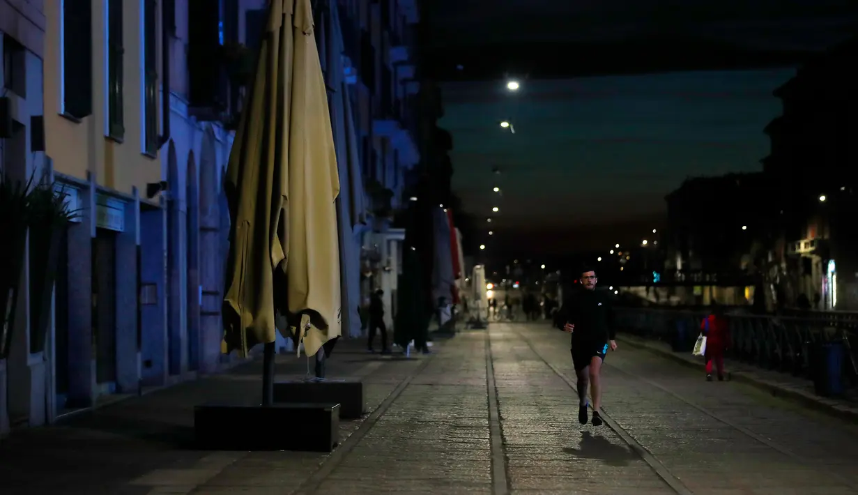 Seorang pria berlari di Kanal Naviglio Grande, Milan, Italia, Selasa (10/3/2020). Untuk mengantisipasi penyebaran virus corona (COVID-19), bar atau restoran hanya diizinkan buka mulai pukul 06.00 sampai 18.00. (AP Photo/Antonio Calanni)