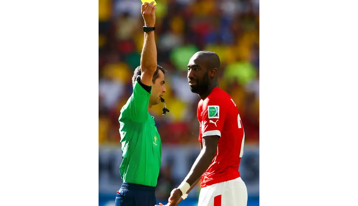 Pemain belakang Timnas Swiss, Johan Djourou (kanan) harus menerima kartu kuning dari wasit, Ravshan Irmatov, saat berlaga di laga penyisihan Piala Dunia 2014 Grup E di Estádio Nacional de Brasilia, (15/6/2014). (REUTERS/Eddie Keogh)