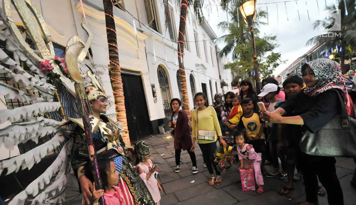 Pengunjung berfoto dengan wanita yang mengenakan kostum di kawasan wisata Kota Tua, Jakarta, Selasa (27/6). Memasuki libur lebaran hari ke-3, kawasan wisata Kota Tua penuh dikunjungi warga. (Liputan6.com/Yoppy Renato)