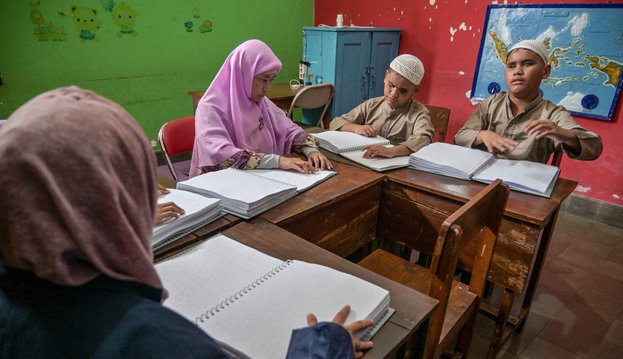Melalui pendampingan guru, para siswa mempelajari dan memperdalam kemampuan membaca Al Quran menggunakan huruf Braille yang dirancang khusus bagi penyandang tunanetra. Tampak dalam foto, para siswa tunanetra membaca Al-Quran dalam huruf Braille selama bulan suci Ramadan 1447 Hijriah di sebuah sekolah di Surabaya, Jawa Timur, pada 27 Februari 2026. (JUNI KRISWANTO/AFP)