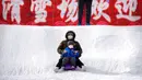Seorang wanita dan anak-anak yang mengenakan masker meluncur menuruni bukit tertutup salju menggunakan kereta luncur di taman umum saat pekan liburan Tahun Baru Imlek di Beijing, China, Kamis (26/1/2023). (AP Photo/Mark Schiefelbein)