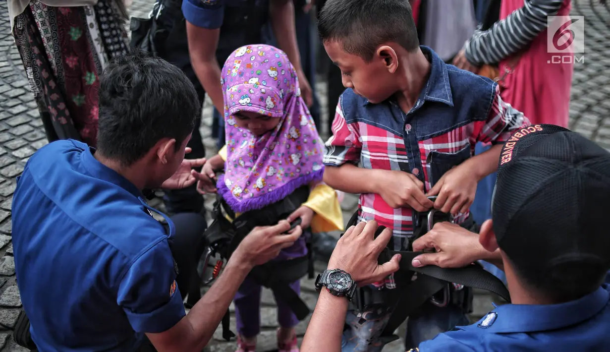 Petugas pemadam kebakaran memasang alat pengaman pada tubuh anak yang akan mencoba wahana flying fox di area Monas, Jakarta, Selasa (1/1). Pengunjung dapat menikmati wahana ini secara gratis. (Liputan6.com/Faizal Fanani)