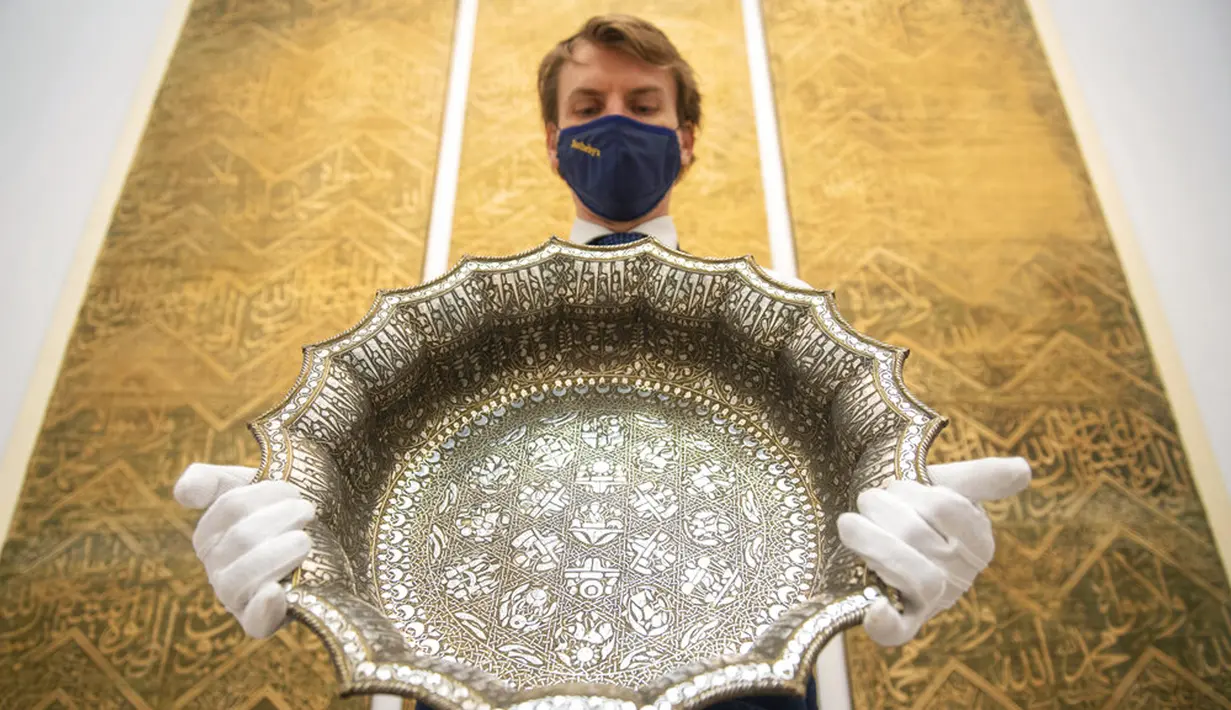 Karyawan rumah lelang Sotheby memegang baskom bergigi perak abad ke-12 dengan desain astrologi, diperkirakan berharga 1.000.000-1.500.000 poundsterling, sebagai bagian dari penjualan Arts of the Islamic World dan India pada 31 Maret di London, Inggris, Senin (29/3/2021). (Dominic Lipinski/PA via AP)