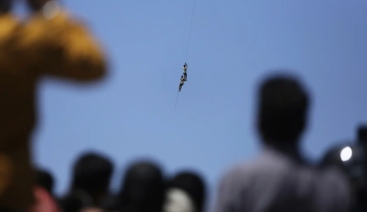 Warga menyaksikan dua nelayan India berpegangan pada tali ketika mereka diselamatkan oleh helikopter Angkatan Udara India dari banjir di Sungai Tawi di Jammu, India (19/8/2019). Dua nelayan selamat kemudian berenang ke tempat yang aman. (AP Photo/Channi Anand)