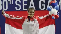 Lifter Windy Aisyah mengibarkan bendera usai mendapatkan medali emas SEA Games 2019 cabang angkat besi nomor 49 kg di Stadion Rizal Memorial, Manila, Minggu (1/12). Dirinya meraih emas dengan total angkatan 104 kg. (Bola.com/M Iqbal Ichsan)
