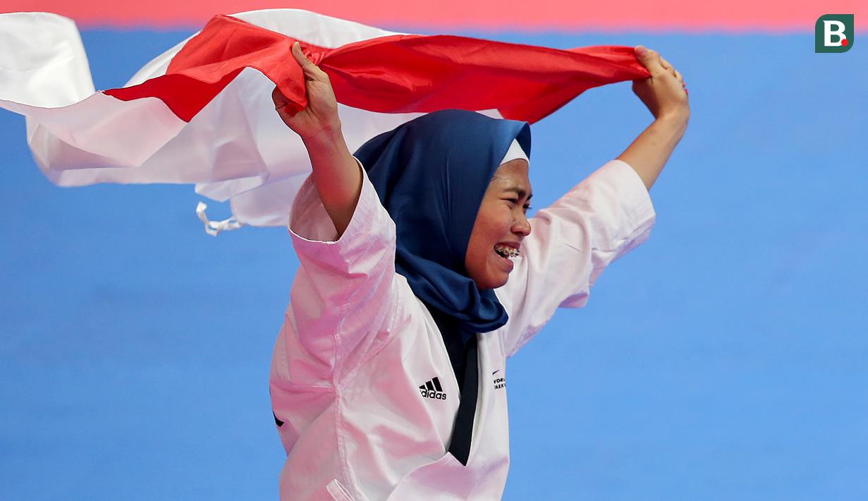 Atlet taekwondo, Defia Rosmaniar, melakukan selebrasi usai berhasil meriah medali emas pertama untuk Indoensia di Asian Games 2018 di JCC, Jakarta, Minggu (19/8/2018). (Bola.com/Peksi Cahyo)