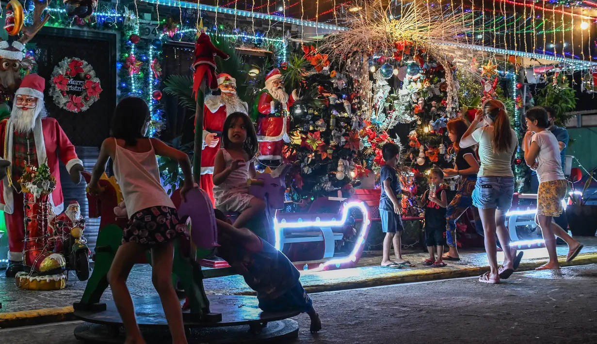 Anak-anak bermain di luar rumah bertema Natal di Manila (21/12/2022). Perayaan Natal tinggal menghitung hari, warga Manila antusias mengunjungi rumah yang didekor dengan ornamen dan hiasan Natal itu. (AFP/Jam Sta Rosa)