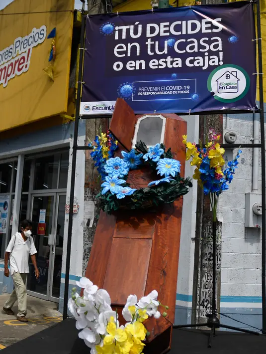 Warga berjalan dekat peti mati dengan tulisan, "Anda memutuskan, di rumah atau di dalam kotak ini", sebagai bagian dari kampanye pemerintah setempat di jalan-jalan kotamadya Escuintla, Guatemala City pada 21 Juli 2020. Kampanye itu sebagai upaya menghentikan penyebaran COVID-19. (Johan ORDONEZ/AFP)