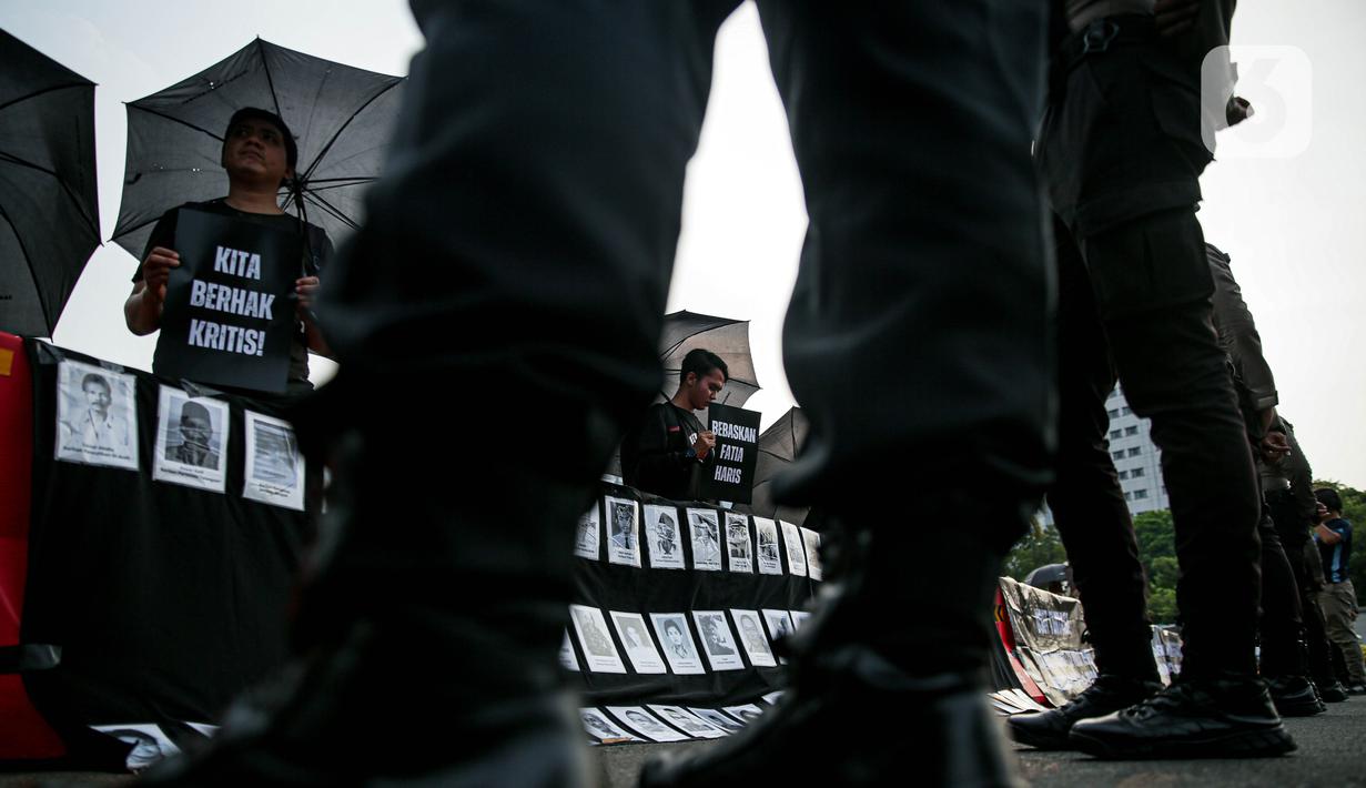 Anggota Jaringan Solidaritas Korban untuk Keadilan (JSKK) menggunakan payung hitam sambil membawa poster bertuliskan pesan-pesan dan menampilkan foto para korban pelanggaran HAM saat melakukan Aksi Kamisan ke-795 di seberang Istana Merdeka, Jakarta, Kamis (16/11/2023). (Liputan6.com/Faizal Fanani)