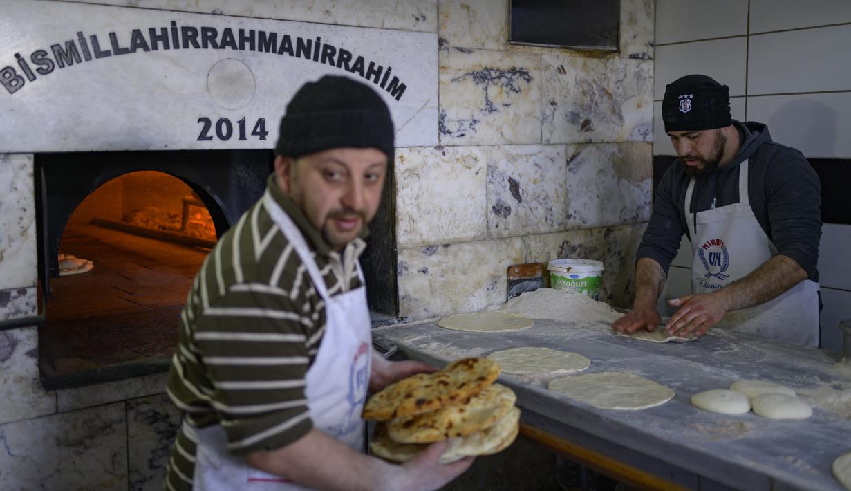 Para pekerja mengumpulkan roti di toko roti yang membagikan roti gratis di Samandag, selatan Hatay pada 16 Februari 2023, sepuluh hari setelah gempa berkekuatan 7,8 melanda wilayah perbatasan Turki dan Suriah.  Lusinan tangan dengan panik meraih pemanas dan selimut yang dibagikan oleh donor swasta, menggambarkan keputusasaan dan kemarahan yang mencengkeram wilayah Turki 11 hari setelah bencana gempa. (Photo by Yasin AKGUL / AFP)