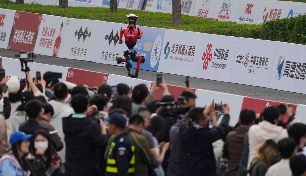 Untuk pertama kalinya, robot humanoid berkompetisi secara resmi berdampingan dengan ribuan pelari manusia dalam lintasan sejauh 21,0975 km. Tampak dalam foto, para jurnalis merekam saat sebuah robot berkompetisi dalam Beijing E-Town Half Marathon dan Humanoid Robot Half-Marathon yang diadakan di pinggiran Beijing, Minggu 19 April 2026. (AP Photo/Andy Wong)