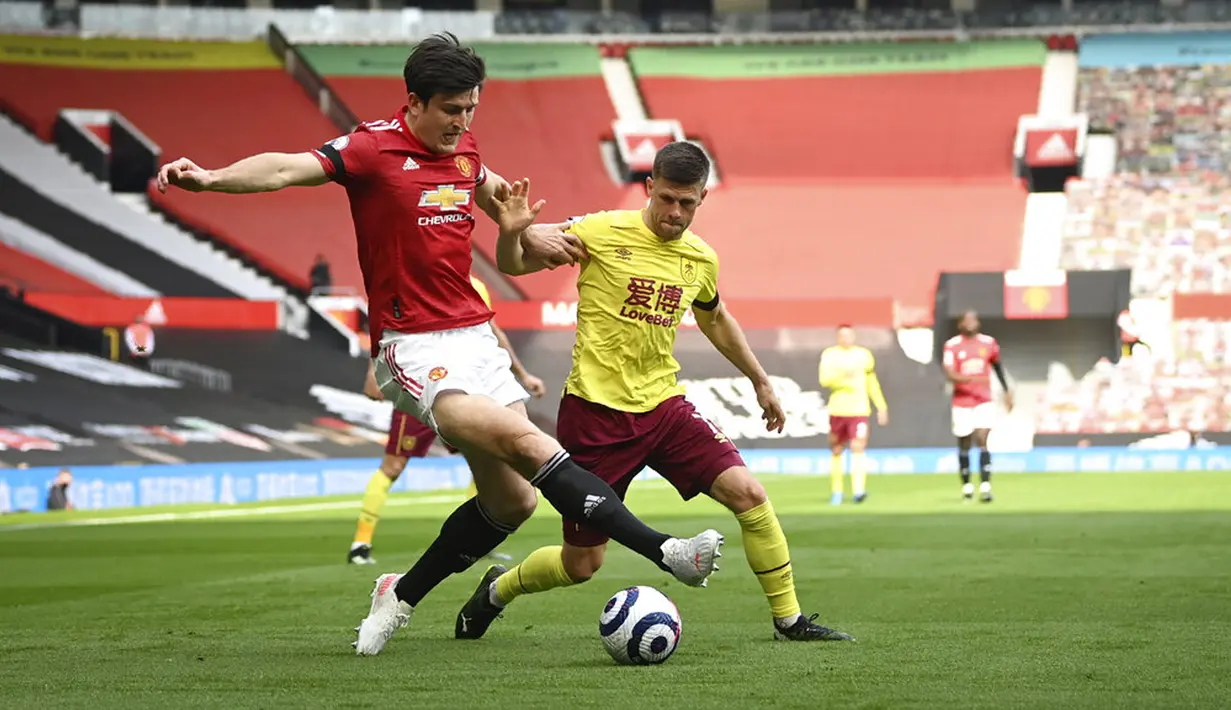 Pemain Manchester United Harry Maguire (kiri) berebut bola dengan pemain Burnley Johann Berg Gudmundsson pada pertandingan Liga Inggris di Stadion Old Trafford, Manchester, Inggris, Minggu (18/4/2021). Manchester United menang 3-1. (Gareth Copley/Pool via AP)