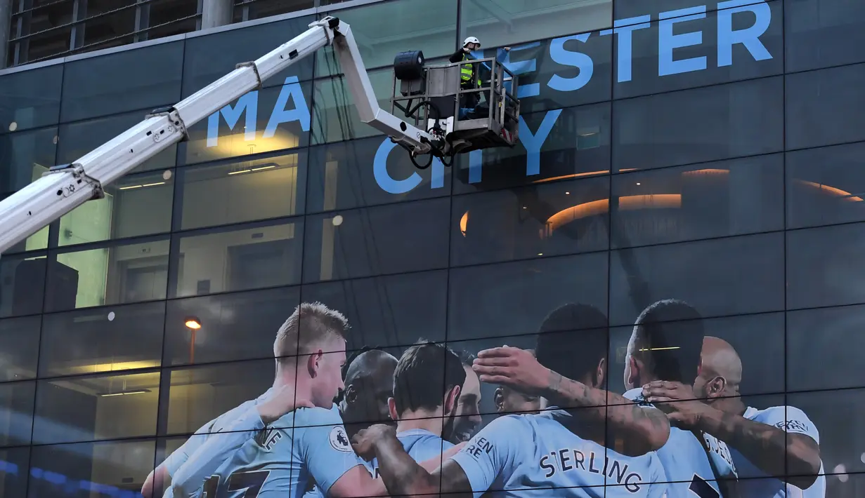 Pekerja memasang poster raksasa bergambar pemain Manchester City terpasang di Stadion Etihad, Manchester, Senin (17/4/2018). Persiapan ini dilakukan untuk merayakan pesta juara Manchester City meraih gelar Premier League. (AFP/Paul Ellis)