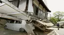 Warga berjalan di depan mobil yang tertimpa reruntuhan rumah di kota Mashiki, Kumamoto, Jepang selatan, Jumat (15/4). Gempa 6,4 SR yang mengguncang pada Kamis (14/4) waktu setempat, mengakibatkan lebih dari 20 bangunan rumah hancur. (REUTERS/Kyodo)