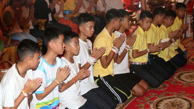 Pelatih tim sepak bola remaja Thailand, Ekkapol Janthawong (empat kanan) bersama 12 anak asuhnya mengikuti ritual setelah berhasil selamat dari dalam gua,  Distrik Mae Sai, Chiang Rai, Kamis (19/7). (AP Photo/Sakchai Lalit)