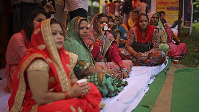 Seorang wanita Hindu India (tengah) minum teh yang dibuat dengan urine sapi selama acara yang diselenggarakan oleh kelompok agama Hindu untuk mempromosikan konsumsi urine sapi sebagai obat bat virus corona Covid-19 di New Delhi, India, Sabtu, (14/3/2020). (AP Photo/Altaf Qadri)