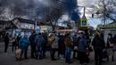 Orang-orang mengantre di depan supermarket sementara asap mengepul di atas kota Vasylkiv di luar Kiev (27/2/2022). Rudal Rusia telah menghantam pipa gas dan kilang minyak di kawasan Vasylkiv. (AFP/Dimitar Dilkof)