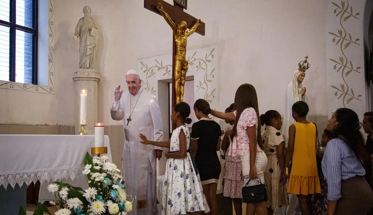 Umat Katolik berkumpul untuk menyentuh potongan karton seukuran Paus Fransiskus, yang saat ini dirawat di rumah sakit di Roma karena pneumonia, dalam misa Minggu di Gereja Santo Antonio de Motael di Dili, Timor Leste, pada 23 Februari 2025. (VALENTINO DARIELL DE SOUSA/AFP)