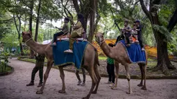 Pengelola Perusahaan Daerah Taman Satwa (PDTS) Kebun Binatang Surabaya (KBS) menyiapkan berbagai wahana ramah anak yang dapat dinikmati selama masa liburan. Tampak dalam foto, anak-anak menunggang unta di Kebun Binatang Surabaya, Jawa Timur, selama libur sekolah sekaligus jelang Natal dan Tahun Baru pada Minggu 21 Desember 2025. (JUNI KRISWANTO/AFP)