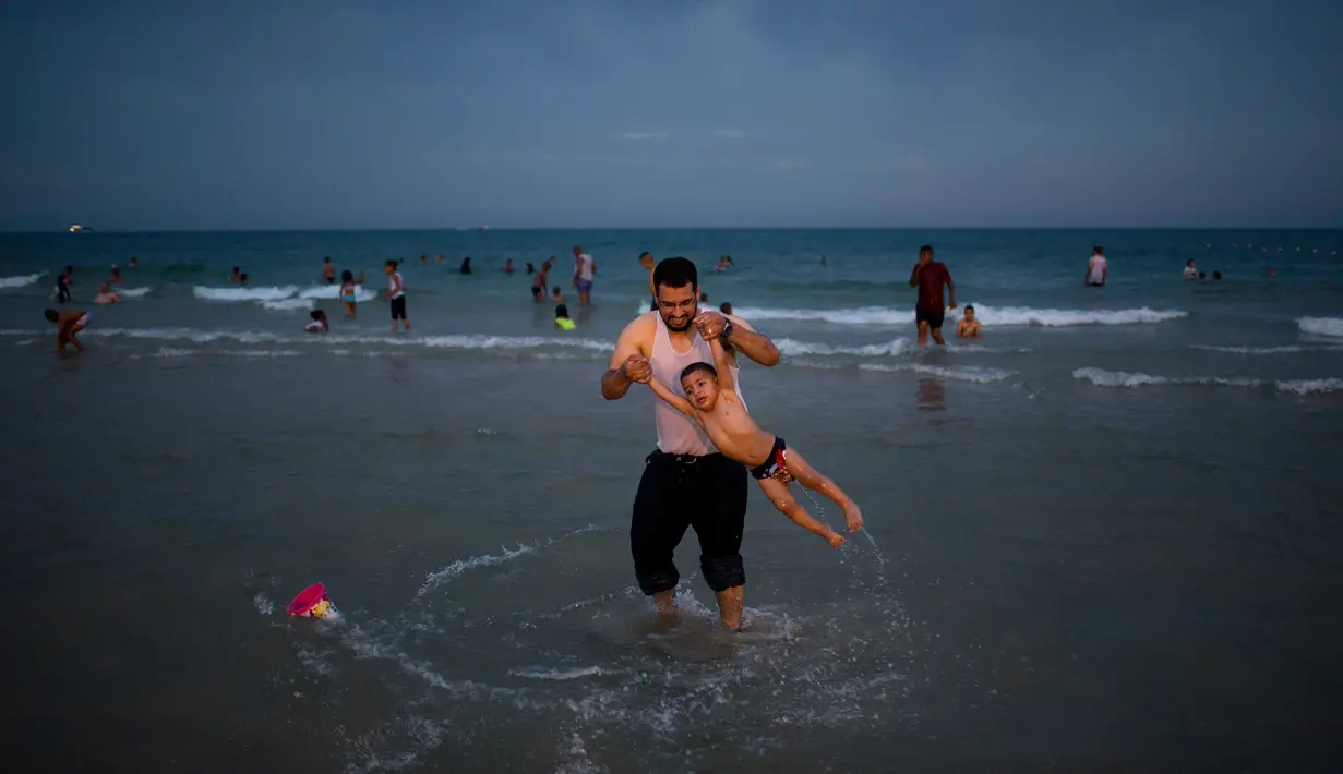 Warga Palestina dan putranya bermain di pantai selama libur Idul Fitri di Tel Aviv, Israel, Sabtu (16/6). (AP Photo/Oded Balilty)