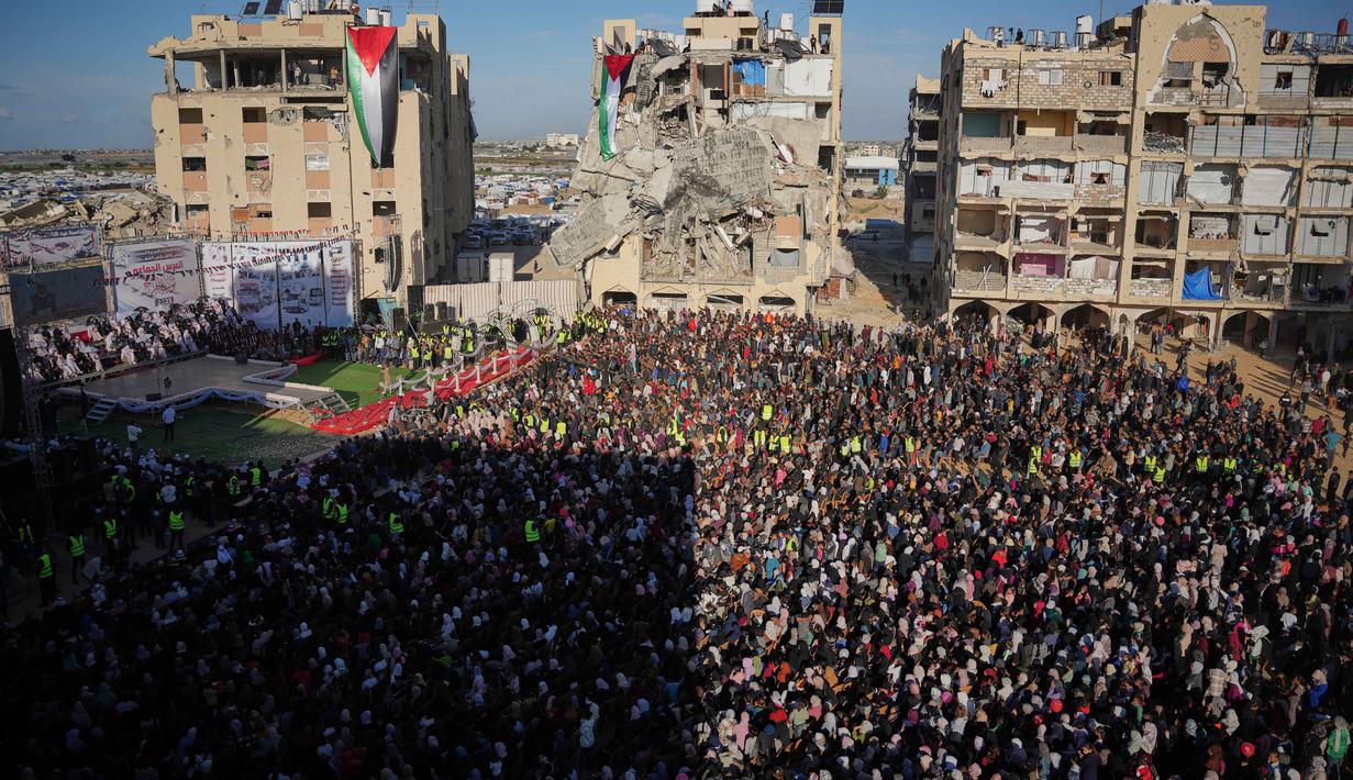 Warga berebut untuk bisa menyaksikan pernikahan tersebut, bahkan sampai memanjat reruntuhan bangunan, untuk menyaksikan upacara tersebut. Tampak dalam foto, warga Palestina menyaksikan dan merayakan upacara pernikahan massal di Kota Hamad, Khan Younis, Jalur Gaza, Selasa 2 Desember 2025. (AP Photo/Abdel Kareem Hana)