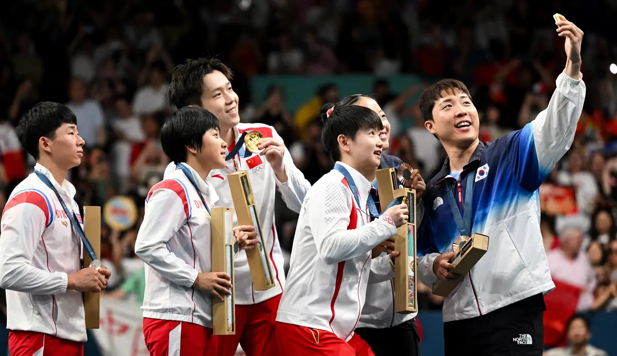 Peraih medali perunggu Lim Jonghoon dari Korea Selatan (kanan) berselfie di atas podium bersama rekan setimnya Shin Yubin, peraih medali emas Wang Chuqin dan Sun Yingsha dari China serta peraih medali perak Ri Jong Sik dan Kim Kum Yong dari Korea Utara pada akhir pertandingan ganda campuran tenis meja Olimpiade Paris 2024 di South Paris Arena, Selasa (30/7/2024). (JUNG Yeon-je / AFP)